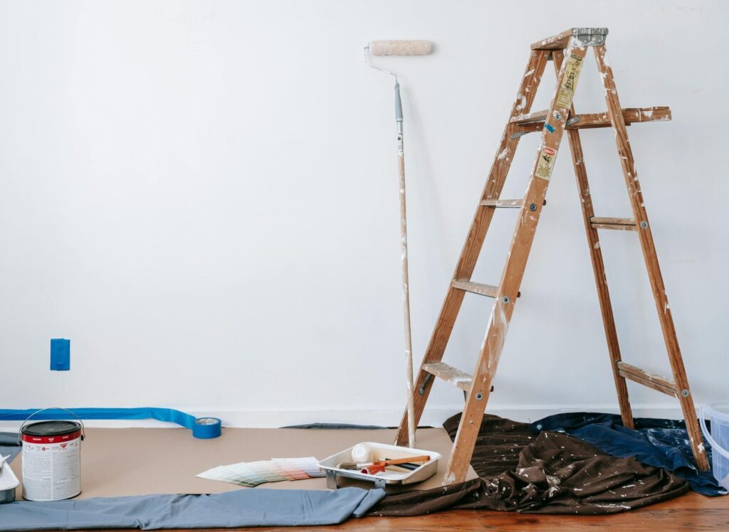 A room prepared for renovation with a ladder, paint supplies, and drop cloth.